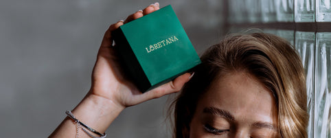 Loretana model holding green branded jewelry box against glass block wall, Baltic silver atelier story from Kaunas. Hallmarked piece.