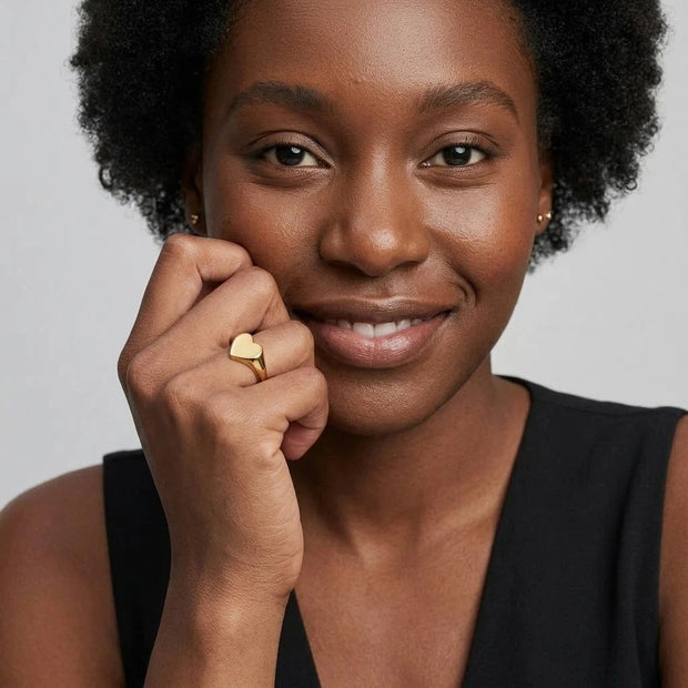 Smiling woman wearing the Engravable Heart Ring in 14K gold-plated 925 silver, hand at her cheek