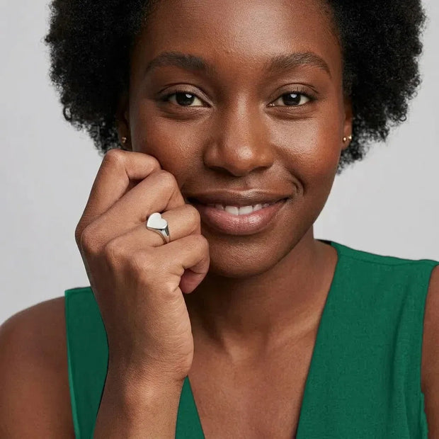 Smiling woman wearing the Engravable Heart Ring in 925 sterling silver, hand at her cheek