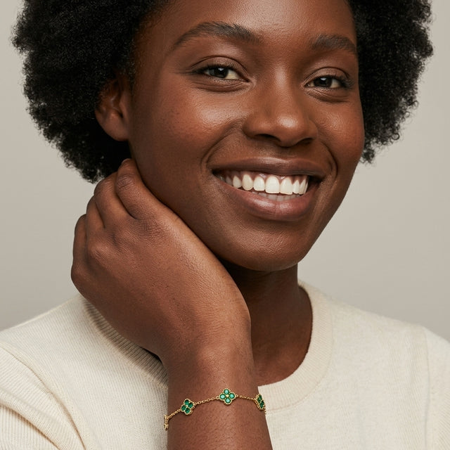 Smiling woman wearing the 14K gold-plated clover bracelet with five green-stone clovers on a fine chain