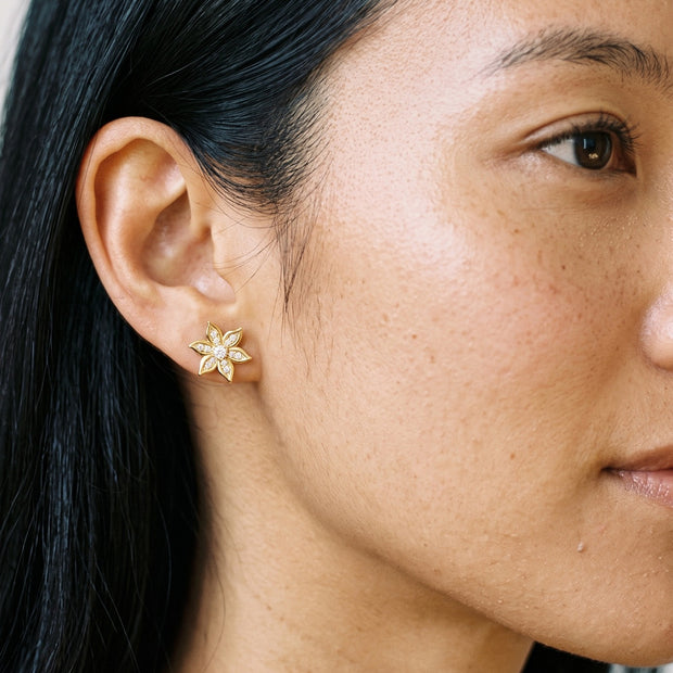 Loretana gold flower stud earring with six petals and clear CZ stones, worn on the ear
