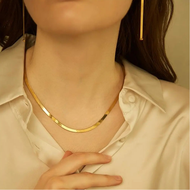 14K zelta plakana čūskas ķēdes kaklarota, stilizēta kopā ar citām smalkām zelta ķēdēm, lai parādītu tās daudzpusību rūpīgi izvēlētā slāņotā komplektā