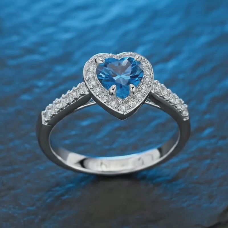 Rotating video of the blue heart zirconia ring in 925 sterling silver with rhodium plating, AAAAA blue sapphire-tone heart-cut stone catching light on a clean white surface. Hallmarked Loretana piece, hand-finished in Kaunas.